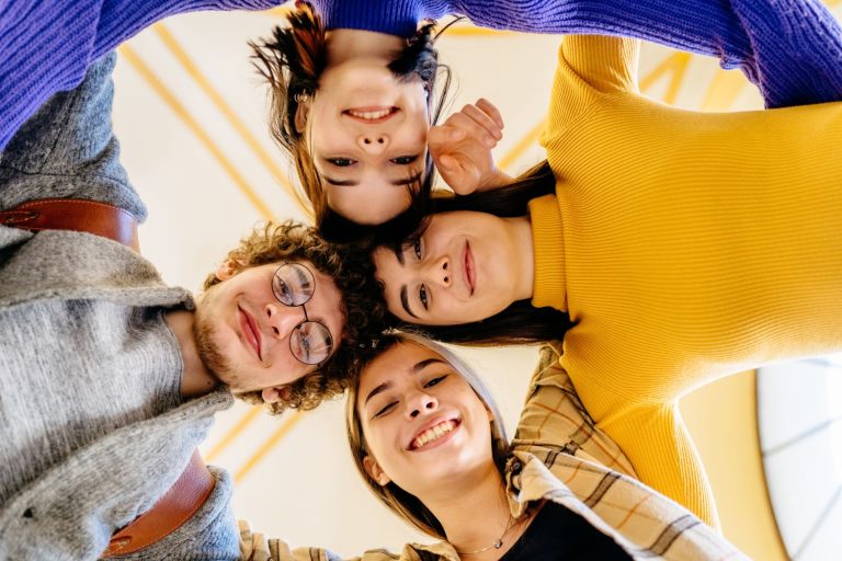 Group of young students standing in a circle, laughing, hugging indoors
