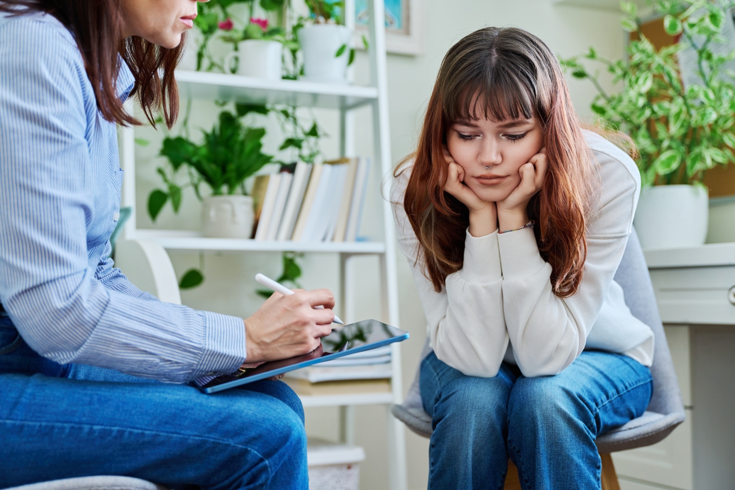 Sad, serious teenage girl at session in office of mental counselor
