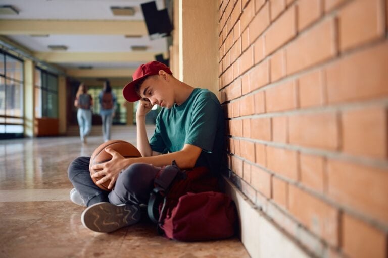 Sad teenage boy sitting alone at high school hallway