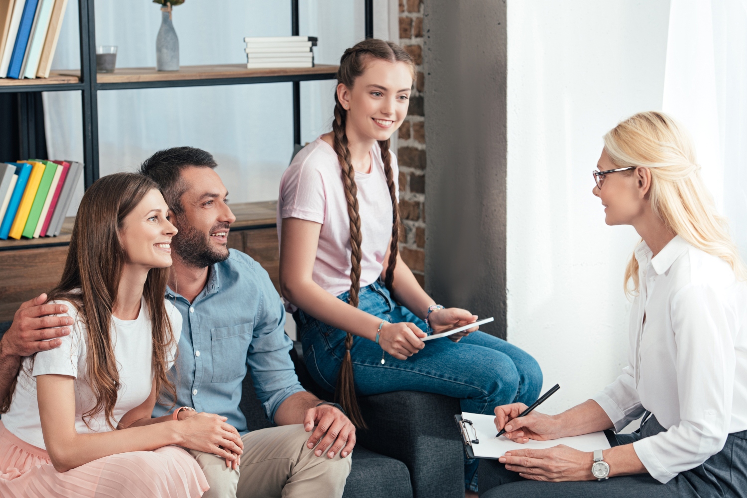 female counselor writing in clipboard on therapy session of family with daughter in office
