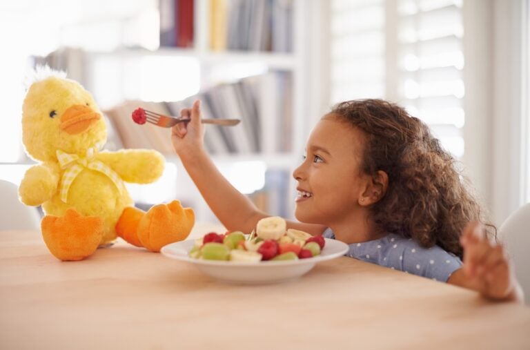 young girl eating and playing with a plush toy