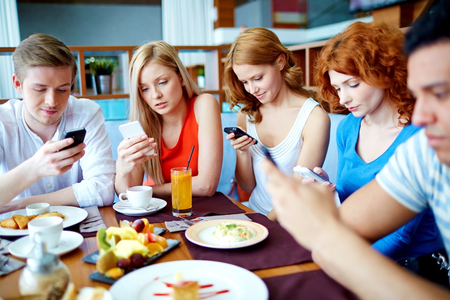 Teenage girls and guys reading sms in cafe