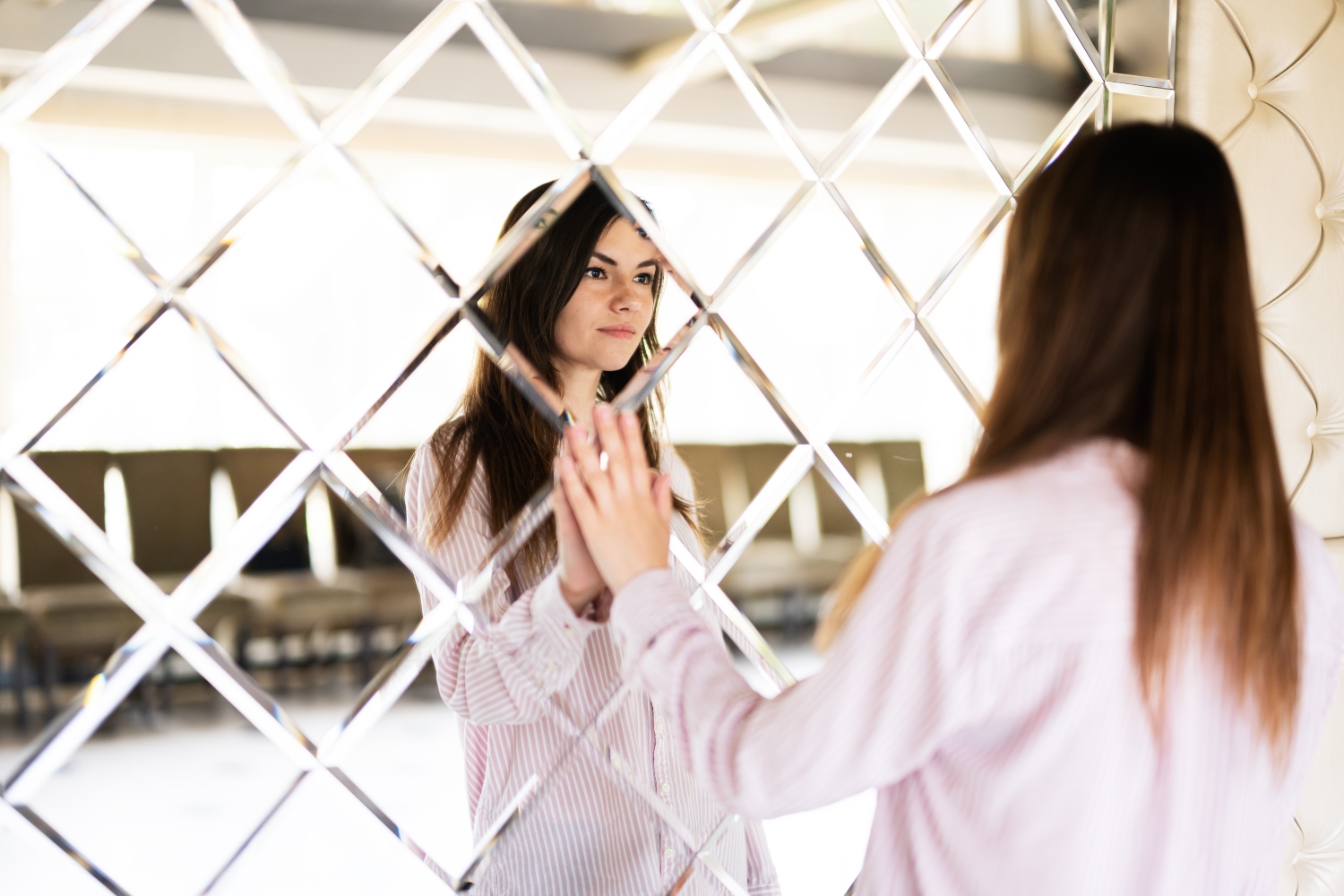 brunette young woman in shirt touching mirror made of rhombuses.
