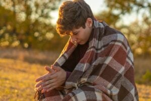 teenage boy huddled in a blanket showing emotional struggle or distress