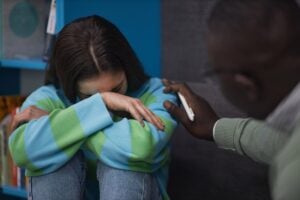 Close up of teenage girl crying in therapy session with psychologist supporting