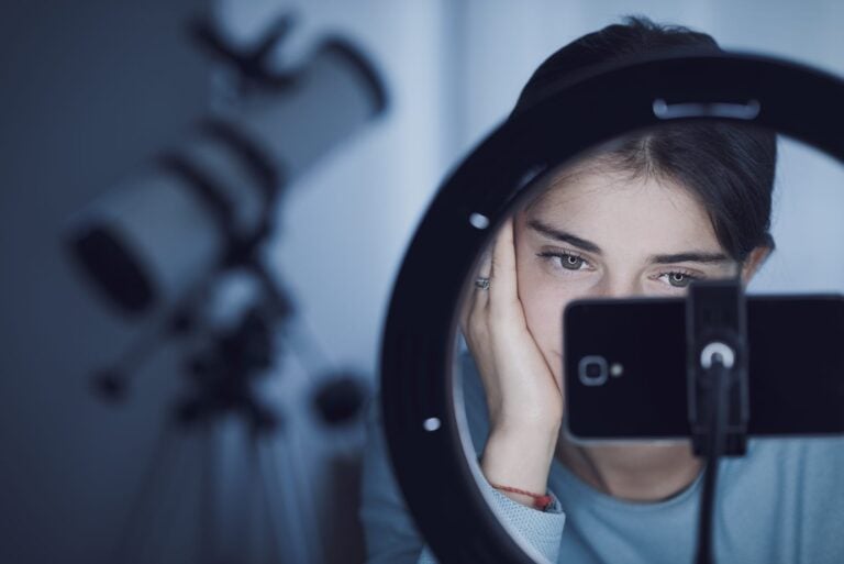 close up shot of a teenage girl looking at her mobile phone connected to a studio ring light