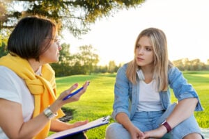 Conversation of young woman with psychologist, social worker, outdoor at meeting in park on lawn