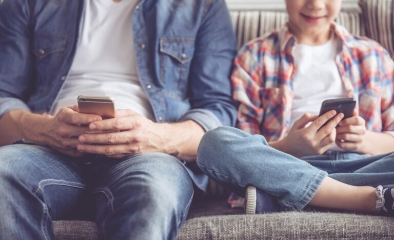 father and son sitting side by side, using mobile phones