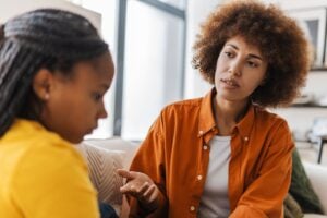 mother speaking with her teenage daughter on sofa at cozy home