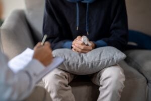 young man sitting on a sofa, clasping his hands together during a mental health counseling session