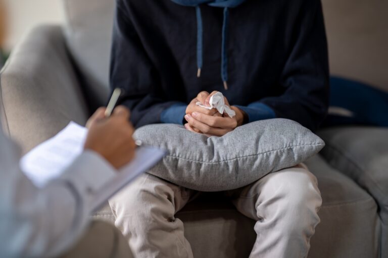 young man sitting on a sofa, clasping his hands together during a mental health counseling session