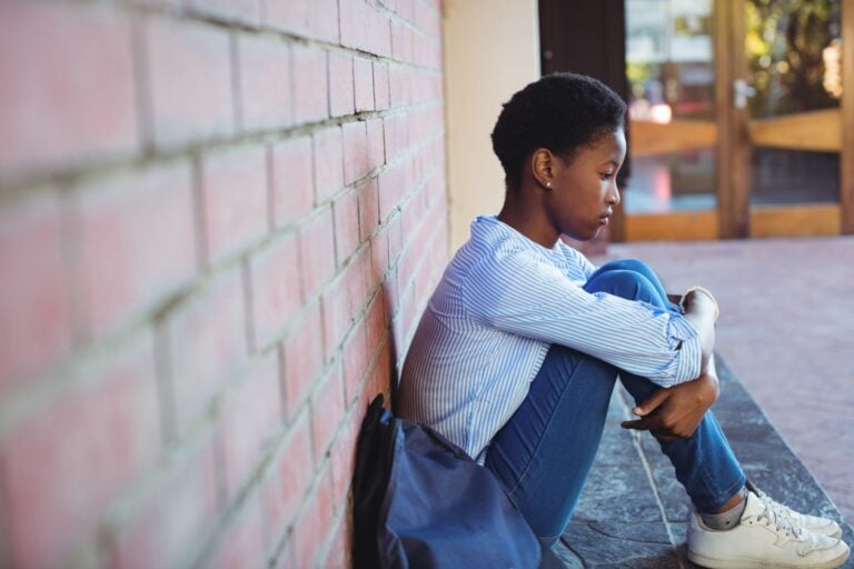 Sad Schoolgirl Sitting Against Brick Wall In School Campus