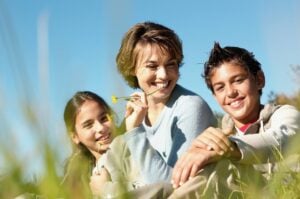 two teenagers sitting beside mother in a field, concept of happiness and family relationships